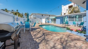 A pool area with a barbecue grill, outdoor seating, and a building with a white facade. - Coastal Getaway Retreat–Steps to the Beach! Studio/1BA. Sleeps 2. In 4-Plex.Pool (Bradenton Beach)