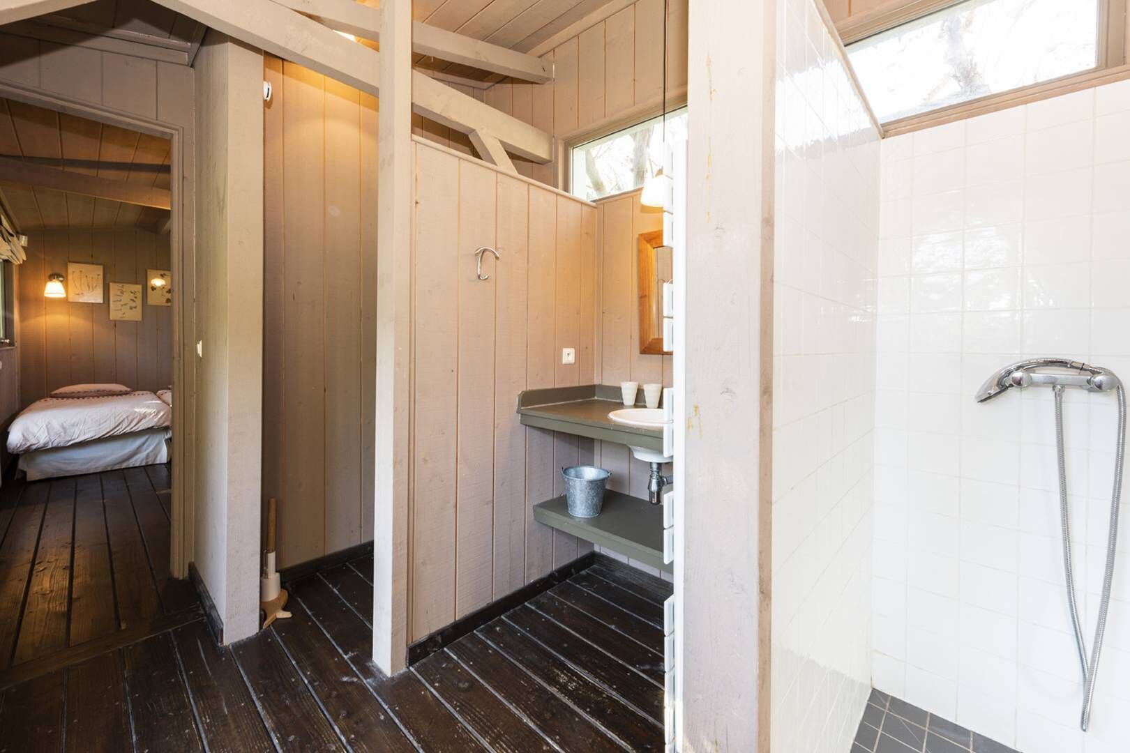 A wooden interior with a bed, a sink, and a shower.