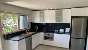 A modern kitchen with white cabinets, a black countertop, stainless steel appliances, and a window providing a view of the outdoors.