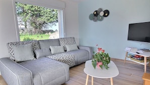 A modern living room with a grey sofa, a white coffee table, and a TV stand with books and a remote control. - Ty Roc'h Lanmodez (sleeps 6) (LANMODEZ)