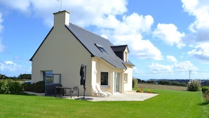 A single-story house with a sloped roof, a chimney, and a patio area with outdoor furniture. - Ty Roc'h Lanmodez (sleeps 6) (LANMODEZ)