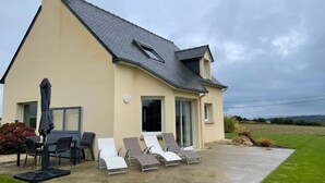 A two-story house with a sloped roof, a covered patio with lounge chairs, and a small garden area. - Ty Roc'h Lanmodez (sleeps 6) (LANMODEZ)