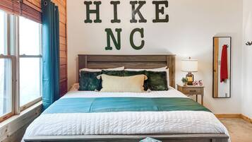 A neatly arranged bed with a headboard, a bedside table with a lamp, and a mirror on the wall.