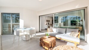 A modern living room with a sofa, coffee table, and dining area. - Jardines - Adama 1.3 POOL VIEW (Arona)