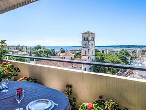 A balcony with a table set for dining, overlooking a cityscape with a prominent tower and a view of the sea.