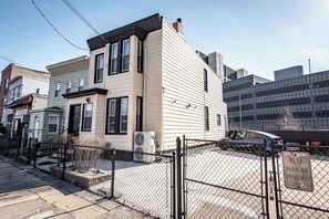 Une maison à deux étages avec une allée bordée d’une clôture, un panneau interdisant le stationnement et une voiture garée au fond.