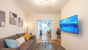 A modern living room with a flat-screen TV, a brown sofa with patterned cushions, a glass coffee table, and abstract wall art. - Chic & Comfortable 1 bed apt with Parking. Walking distance JSQ path. Sleeps 4.  (Jersey City)