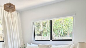 Ein Schlafzimmer mit einem großen Bett, einem Nachttisch, einer Lampe und einem Fenster mit Blick auf Grünflächen.