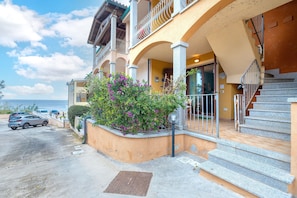 A building with a balcony, a staircase, and a parking area.