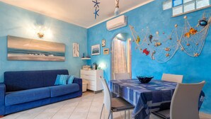 Una habitación con pared azul, un sofá, una mesa de comedor con sillas, una lámpara en el techo y decoración en las paredes.