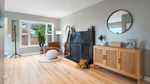 A modern living room with a fireplace, wooden flooring, a large window, and a mirror on the wall. - 3BR 3BA Kerry Park Retreat in Queen Anne, Near Stadium (Seattle)