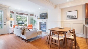 Een ruime woonkamer met een open haard, een eethoek met houten stoelen en een gezellig zitgedeelte met een bank en fauteuils.