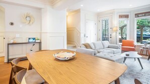 Een moderne woonkamer met een houten eettafel, een grijze bank en een oranje fauteuil.