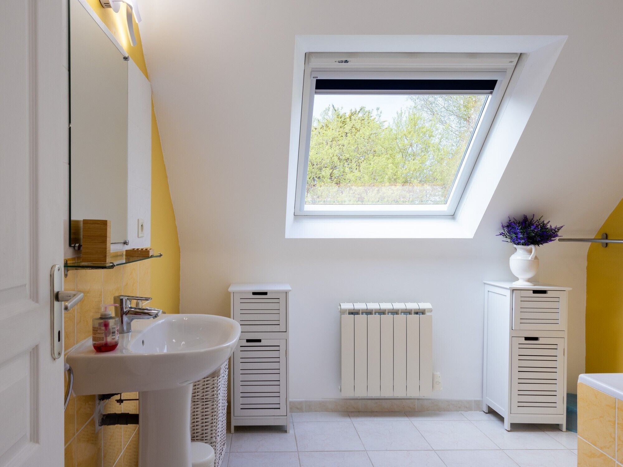 Ein modernes Badezimmer mit Oberlicht, einem weißen Waschbecken, einem Spiegel und einer Heizung.