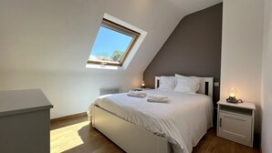 A bedroom with a skylight, a bed with pillows, a bedside table with a lamp, and a nightstand with a lamp. - 'Maison De Charlie' by Madame est Servie – private terrace, garden, and Wi-Fi (Trégastel)