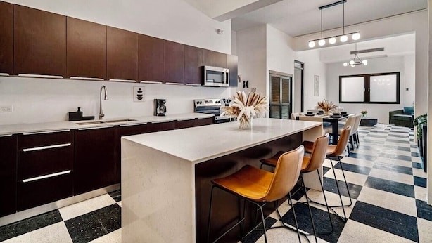 Una cocina moderna con armarios oscuros, encimera blanca y una isla central con taburetes de bar.