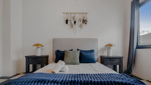 Un dormitorio con una cama grande, dos mesitas de noche, un cabecero y un adorno en la pared.