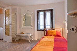 Une chambre à coucher avec un lit, une table de chevet, un miroir et une fenêtre avec des rideaux.