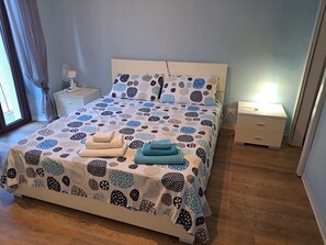 Un lit bien fait, recouvert d’une couvre-lit à motifs, deux tables de chevet avec des lampes et une fenêtre avec des rideaux.