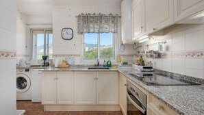 A kitchen with a washing machine, a clock, and a window with a view.