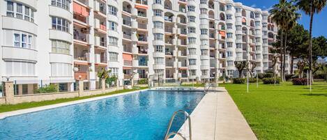 A multi-story hotel with balconies, a swimming pool, and a well-maintained lawn.