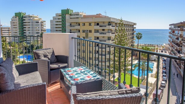 A balcony with wicker furniture, a pool, and high-rise buildings in the background.