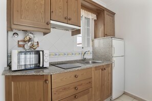 A kitchen with wooden cabinets, a microwave, a refrigerator, and a window with a curtain.