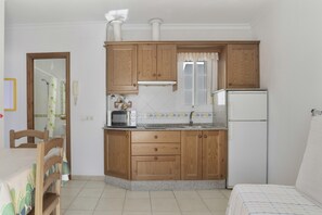 Cocina compacta con armarios de madera, microondas, refrigerador y ventana con cortinas.