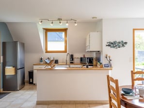 A modern kitchen with a central island, a refrigerator, and a dining area with a table and chairs.
