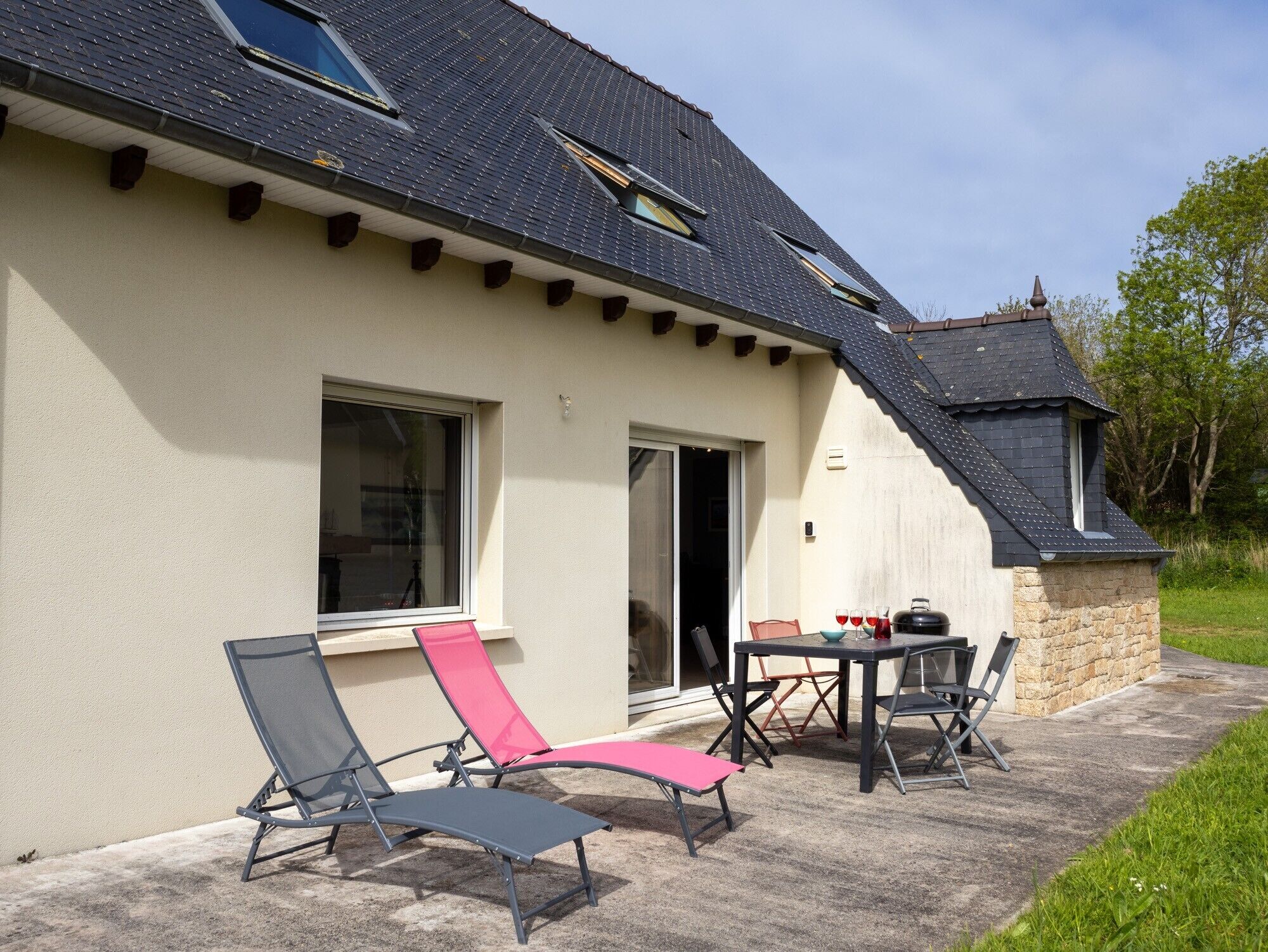 Une maison dotée d’un patio, de deux chaises longues, d’une table et d’un barbecue.