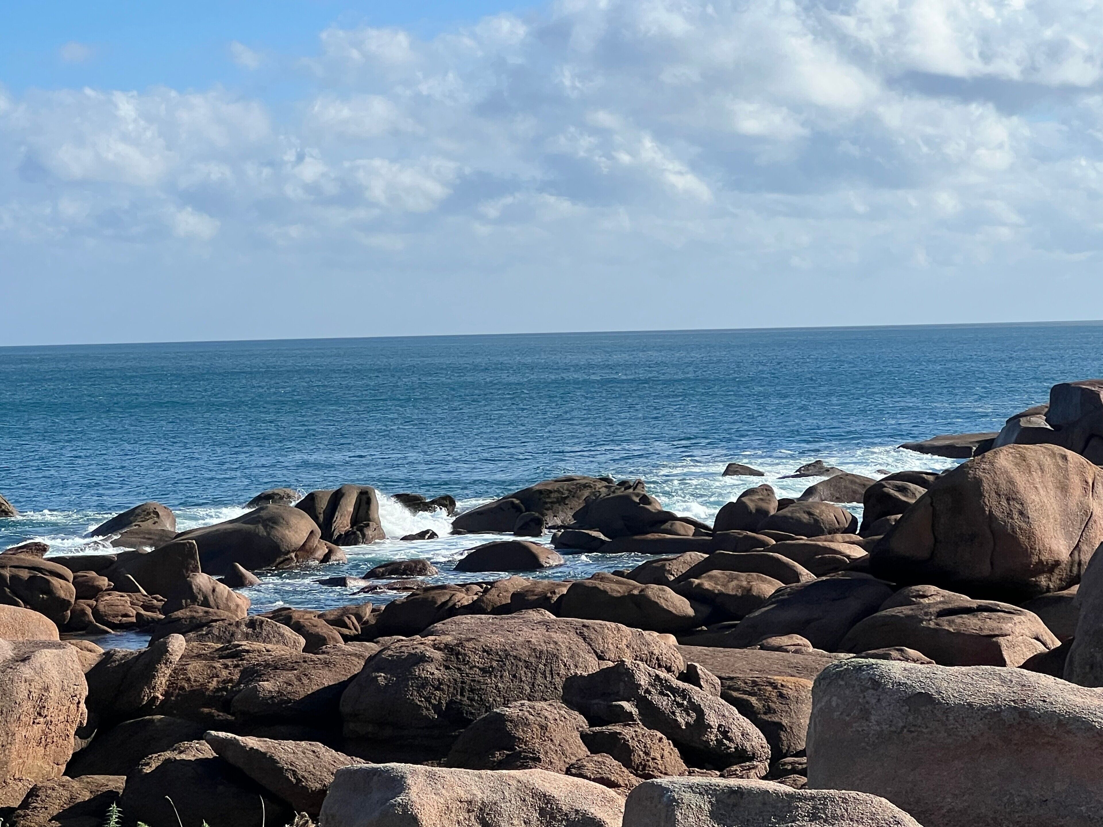 A rocky shoreline with waves crashing against the rocks under a clear sky.