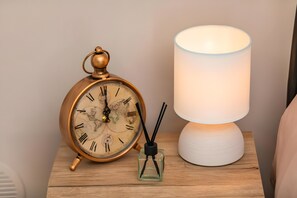 Et natbord i træ med et klokkeuret i vintage-stil, en hvid lampe og en lille glasflaske.