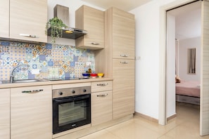 Une cuisine avec un mur recouvert de carreaux, des meubles en bois, un four encastré et une petite plante.
