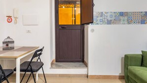 A room with a brown door, a small table with chairs, a green sofa, and a tiled wall.