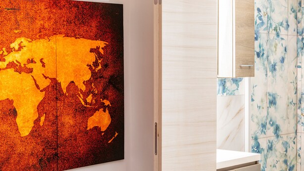 A modern bathroom with a large world map artwork, a wooden cabinet, and a tiled wall with a floral pattern.