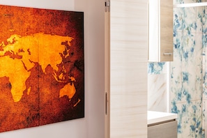 Une salle de bain moderne agrémentée d’une grande œuvre d’art représentant une carte du monde, d’un meuble en bois et d’un mur recouvert de carreaux avec un motif floral.