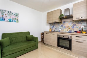 Une cuisine moderne avec un canapé vert, des meubles en bois, un mur recouvert de carreaux et un tableau.