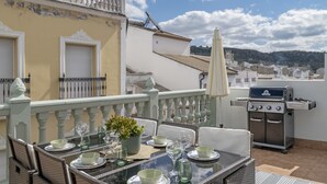 Un balcón con una mesa lista para comer, una parrilla y vistas de la ciudad.