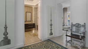 Un pasillo con un tapete estampado, una silla decorativa y un acceso a un baño.