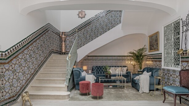 Una imponente escalera con detalles de azulejos intrincados, un espacio de descanso con sofás y reposapiés, y una obra de arte enmarcada de gran tamaño en la pared.