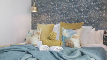 Un lit bien fait, avec une couverture bleue, un coussin décoratif doré et des coussins ornés de motifs floraux.