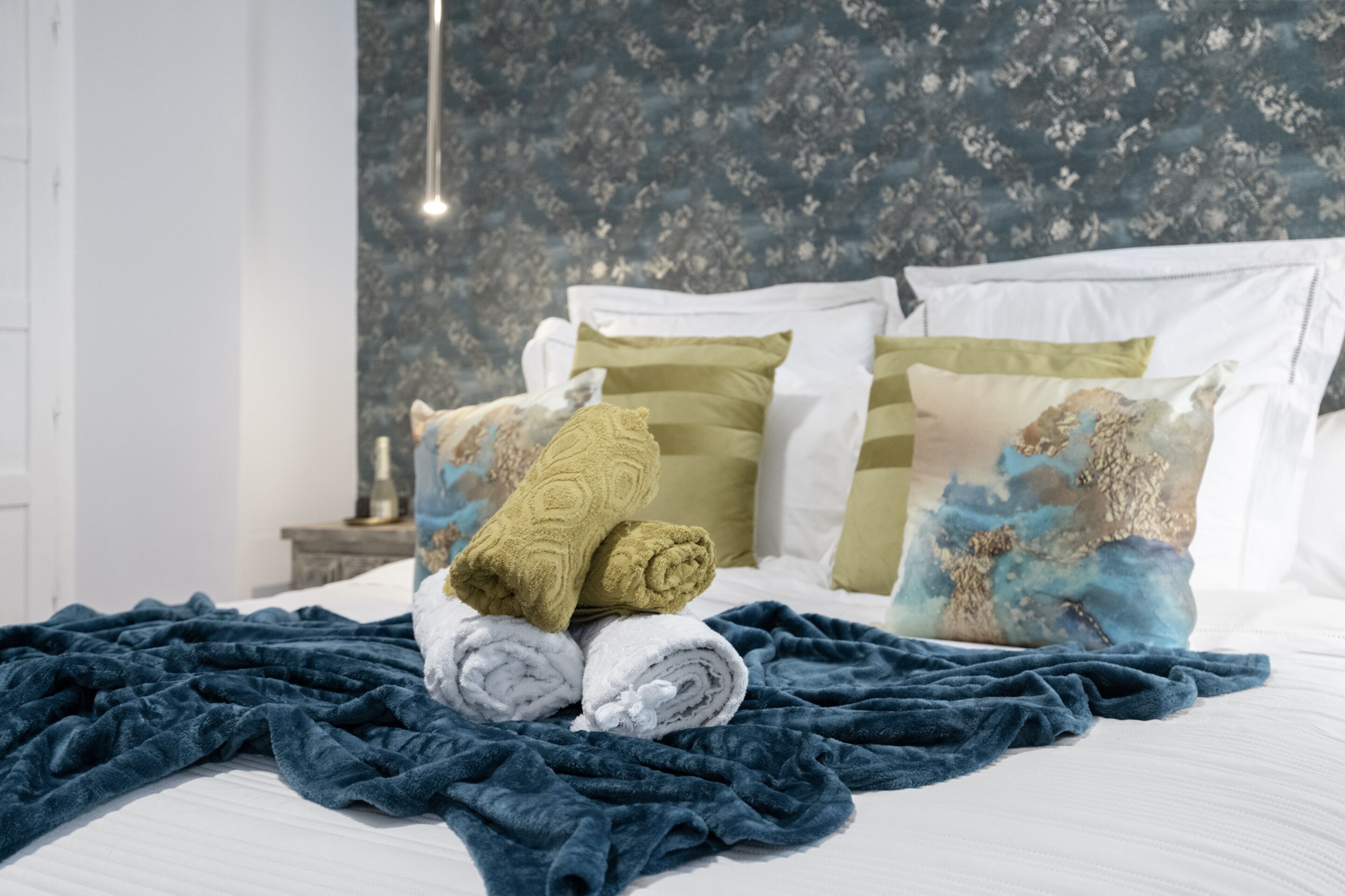 Cama bem arrumada com toalhas dobradas, travesseiros e um cobertor azul escuro.
