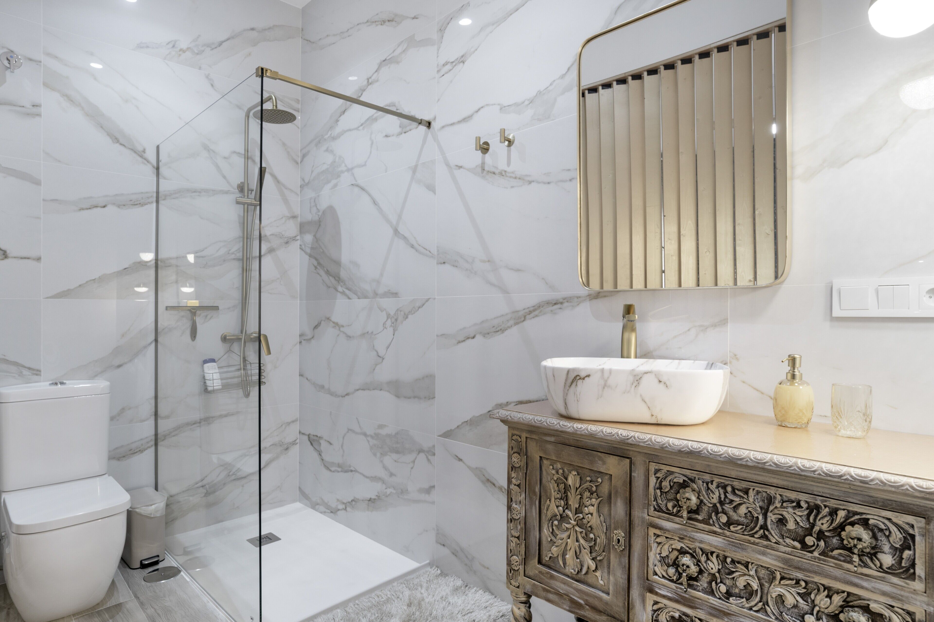 Un baño moderno con ducha envuelta en vidrio, lavamanos de mármol y un mueble decorativo.
