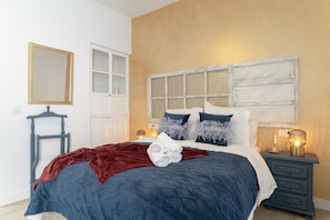 A bedroom with a bed, a nightstand, a dresser, a mirror, and a window with blinds.