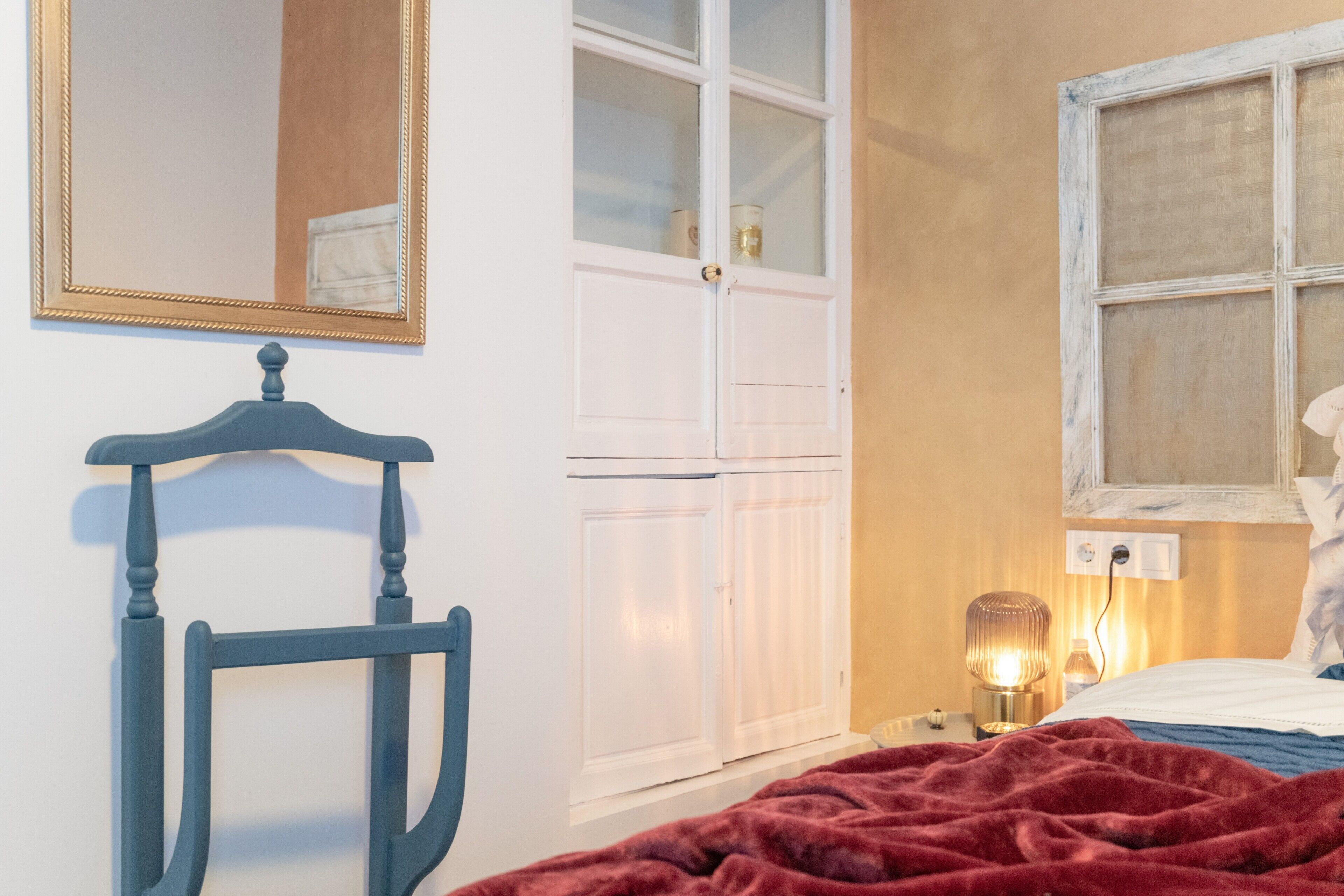 Ein Schlafzimmer mit Bett, Nachttisch, Lampe, Kleiderschrank und Spiegel.