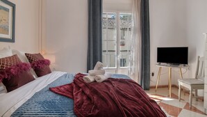 Une chambre à coucher avec un lit, une télévision, une chaise et une fenêtre avec des rideaux.