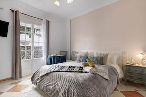 A bedroom with a bed, a bedside table, a lamp, a window with curtains, and a view of buildings outside. - 'Topacio' Room with Mountain Views, Shared Terrace and Wi-Fi (Alcalá del Valle)