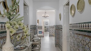 A hallway with patterned tiles, a white vase with flowers, a bench, and a chandelier. - 'Topacio' Room with Mountain Views, Shared Terrace and Wi-Fi (Alcalá del Valle)
