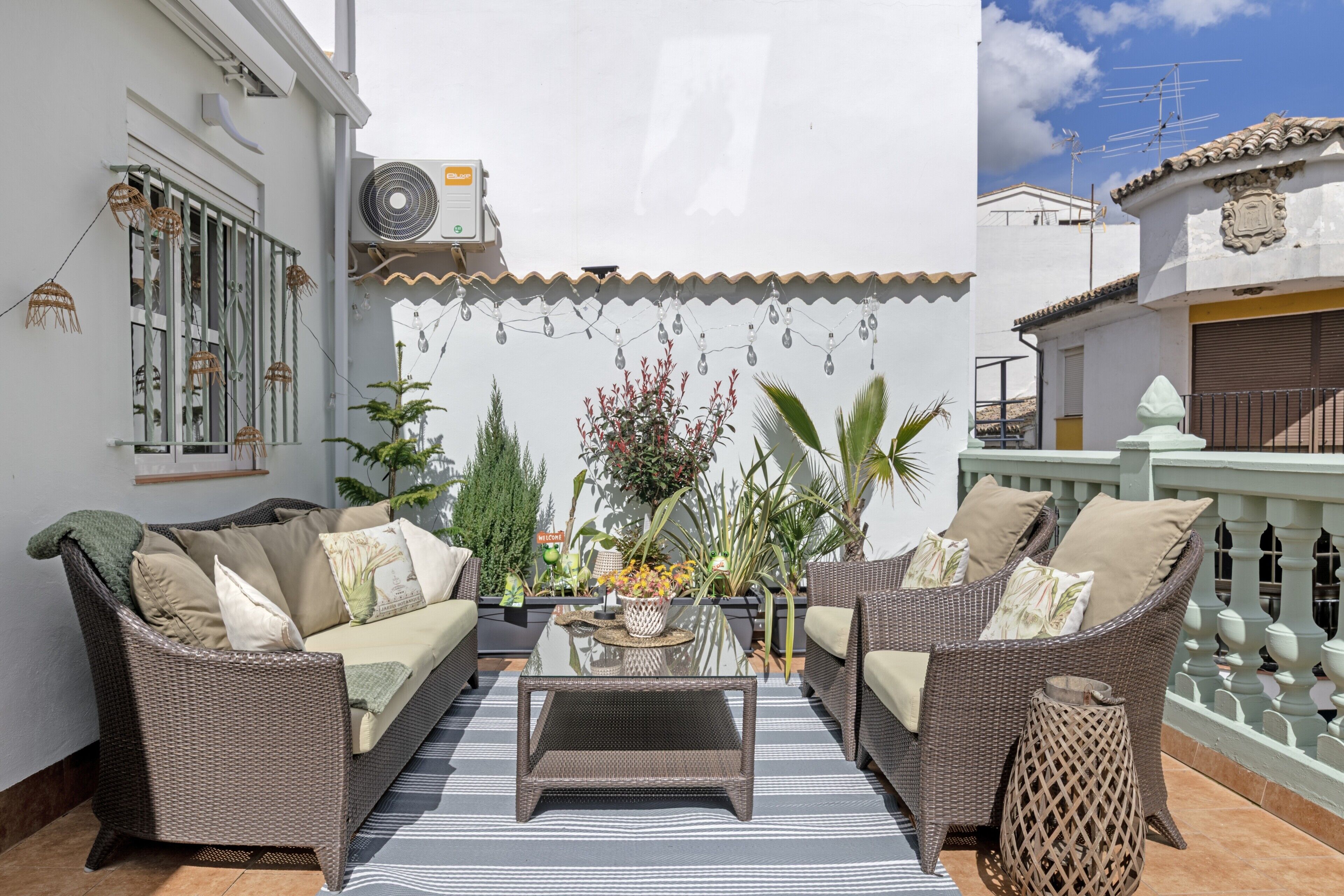 Un patio con mobiliario de mimbre, una mesa de centro de vidrio y plantas en macetas.