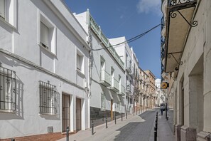 Une rue étroite bordée de bâtiments blancs, dont certains sont dotés de balcons, sous un ciel dégagé.